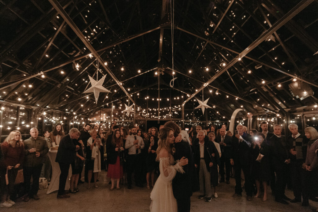 Newlywed couples first dance under a cascade of twinkle lights in a greenhouse beneath the stars